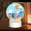 Round Acrylic Night Light, Three People Are Standing On A Beach With Their Surfboards.
